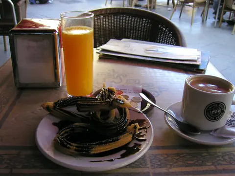 Zumo de naranja, churros y café en la mesa de un bar